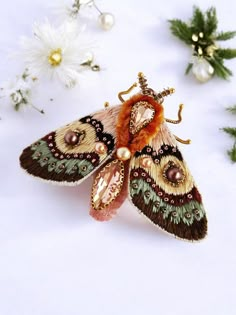 a moth brooch sitting on top of a white surface next to flowers and greenery