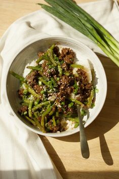 a white bowl filled with meat and vegetables on top of a wooden table next to green onions