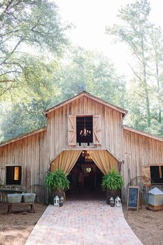 a barn with an open door and curtains on the front, surrounded by greenery