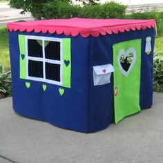 a blue and green play house sitting on top of a cement ground next to bushes