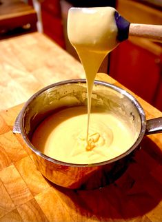 a wooden table topped with a metal pot filled with liquid and cheese being poured into it