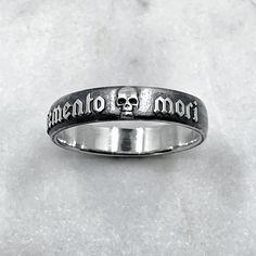 The Memento Mori Ring is not just a piece of jewellery; it is a talisman of empowerment and introspection. By wearing this ring, you carry a symbol of your own mortality, inviting reflection and inspiring a deeper appreciation for the fleeting beauty of life. It serves as a reminder to live fully, embracing the joys and challenges that come your way. Memento mori is a Latin phrase meaning 'remember you must die' Ring is 6mm wide. 925 Sterling Silver. Each piece is handmade to order in our Jewel Spiritual Promise Rings With Engraving Option, Symbolic Skull Ring For Anniversary, Symbolic Etched Jewelry For Promise, Symbolic Engraved Promise Ring, Gothic Engraved Wedding Rings, Gothic Engraved Rings For Anniversary, Symbolic Engraved Ring For Anniversary, Symbolic White Gold Skull Ring For Anniversary, Gothic Engraved Ring Jewelry