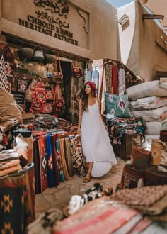 a woman standing in front of a market with lots of rugs and bags on display