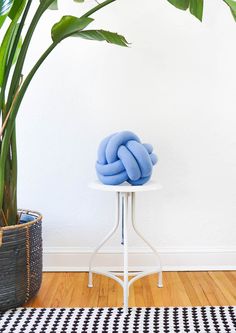 a blue pillow sitting on top of a white table next to a potted plant