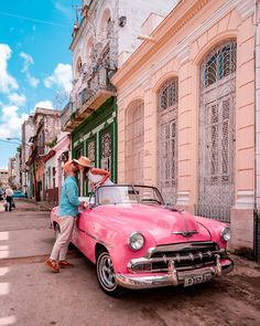 a man leaning on the hood of a pink classic car in front of an old building