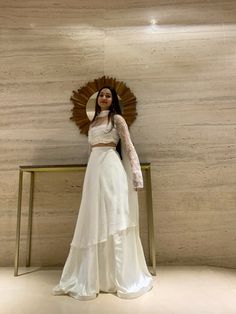 a woman standing in front of a wall wearing a white dress and holding a fan