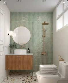 a bathroom with green tiled walls and flooring next to a white toilet sitting under a round mirror