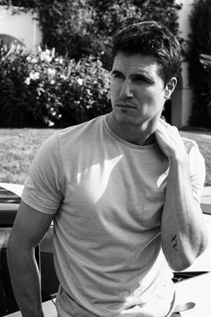 black and white photograph of a man leaning against a car with his hand on his neck