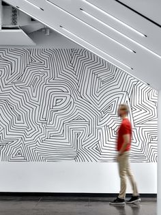 a man walking in front of a white wall with black and white lines on it