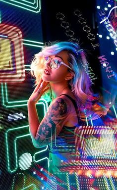 a woman with tattoos and glasses standing in front of neon colored lights on the wall