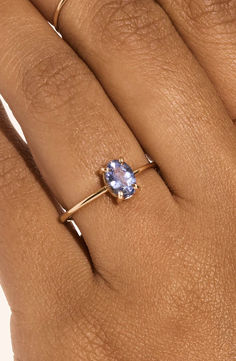 a woman's hand wearing a gold ring with an oval blue stone on it