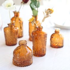 four brown glass vases with flowers in them on a white tablecloth covered table