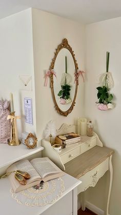 a white desk topped with a mirror next to a shelf filled with books and flowers