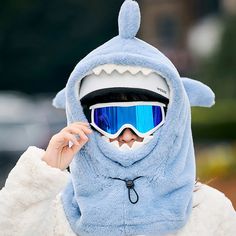 a person wearing a blue shark costume and ski goggles on their head while holding onto his sunglasses