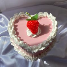 a strawberry on top of a heart shaped cake with white frosting and pink icing