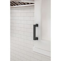 a black handle on a white cabinet door in a room with white tile walls and flooring