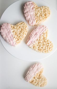 three heart shaped cookies sitting on top of a white plate next to each other with pink icing