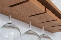 three wine glasses hanging from a wooden shelf