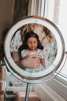 a reflection of a woman holding a doll in front of a mirror on a table