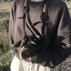 a man holding a camera in his hands while standing on a grass covered field with trees