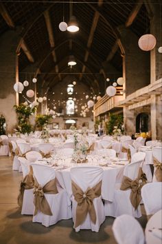 the tables are set with white linens and brown bows on them, along with paper lanterns hanging from the ceiling