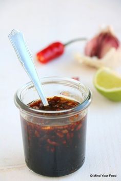 a glass jar filled with chili sauce next to a lime slice and pepper on the side