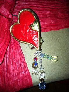 a red and gold heart shaped brooch laying on top of a bed