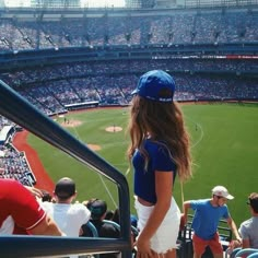 a girl standing in the stands at a baseball game looking out over the field with her hat on