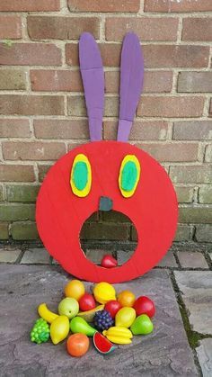 a red letter shaped like a face with fruit in front of it on the ground