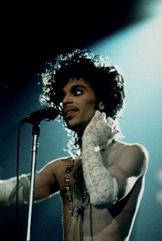 a man with no shirt on holding a microphone in front of his face and wearing white gloves