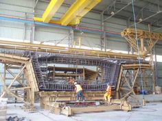 two men working on a large machine in a building with steel pipes and yellow beams