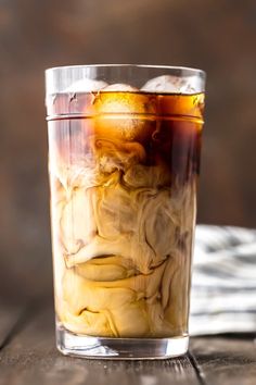 a glass filled with liquid and ice sitting on top of a wooden table