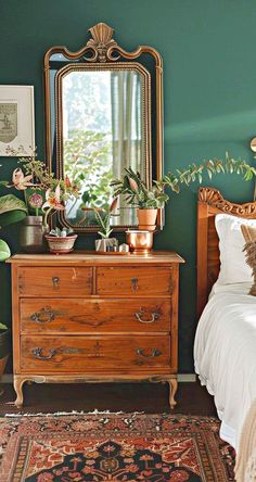 a bedroom with a dresser, mirror and plants on the nightstand in front of it