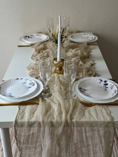 the table is set with white plates and place settings for four people to sit at