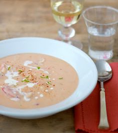 a white bowl filled with soup on top of a table next to two wine glasses