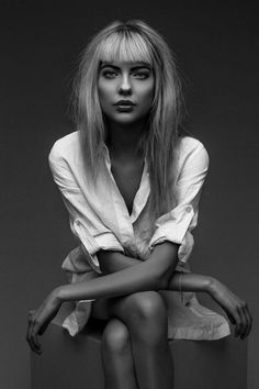 a black and white photo of a woman with blonde hair sitting on a stool, looking at the camera