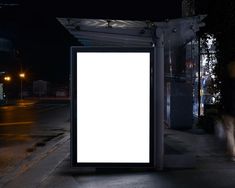 a bus stop at night with a large white billboard on the side of the road