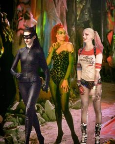 three women dressed in catwoman costumes standing next to each other on a rock ground