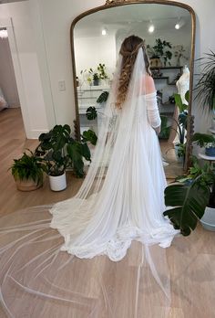 a woman in a wedding dress looking at herself in the mirror with her veil draped over her head