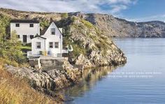 a white house sitting on top of a cliff next to the ocean with mountains in the background