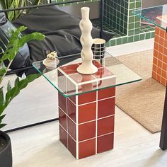 a glass table topped with a vase next to a potted plant and a couch