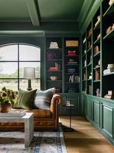 a living room filled with lots of green bookshelves next to a large window