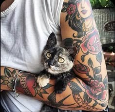 a man holding a cat in his arms with tattoos on it's sleeves and arm