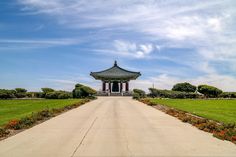 a walkway leading to a small pavilion in the middle of a grassy area with flowers on either side