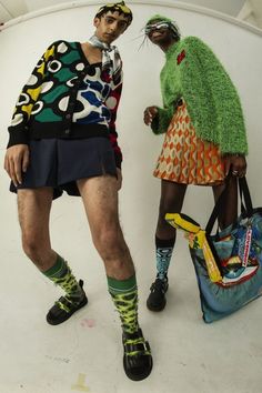 two men standing next to each other in front of a white wall wearing colorful clothing