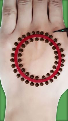 a hand holding a red circle with chocolate balls on it and a pair of scissors