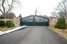 a driveway with a large gate and stone wall on the other side, surrounded by trees