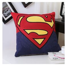 a superman pillow sitting on top of a table next to a coffee cup and framed pictures