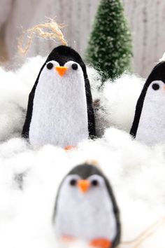 three penguins are standing in the snow next to a christmas tree