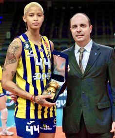 a man in a suit and tie standing next to a basketball player holding an award